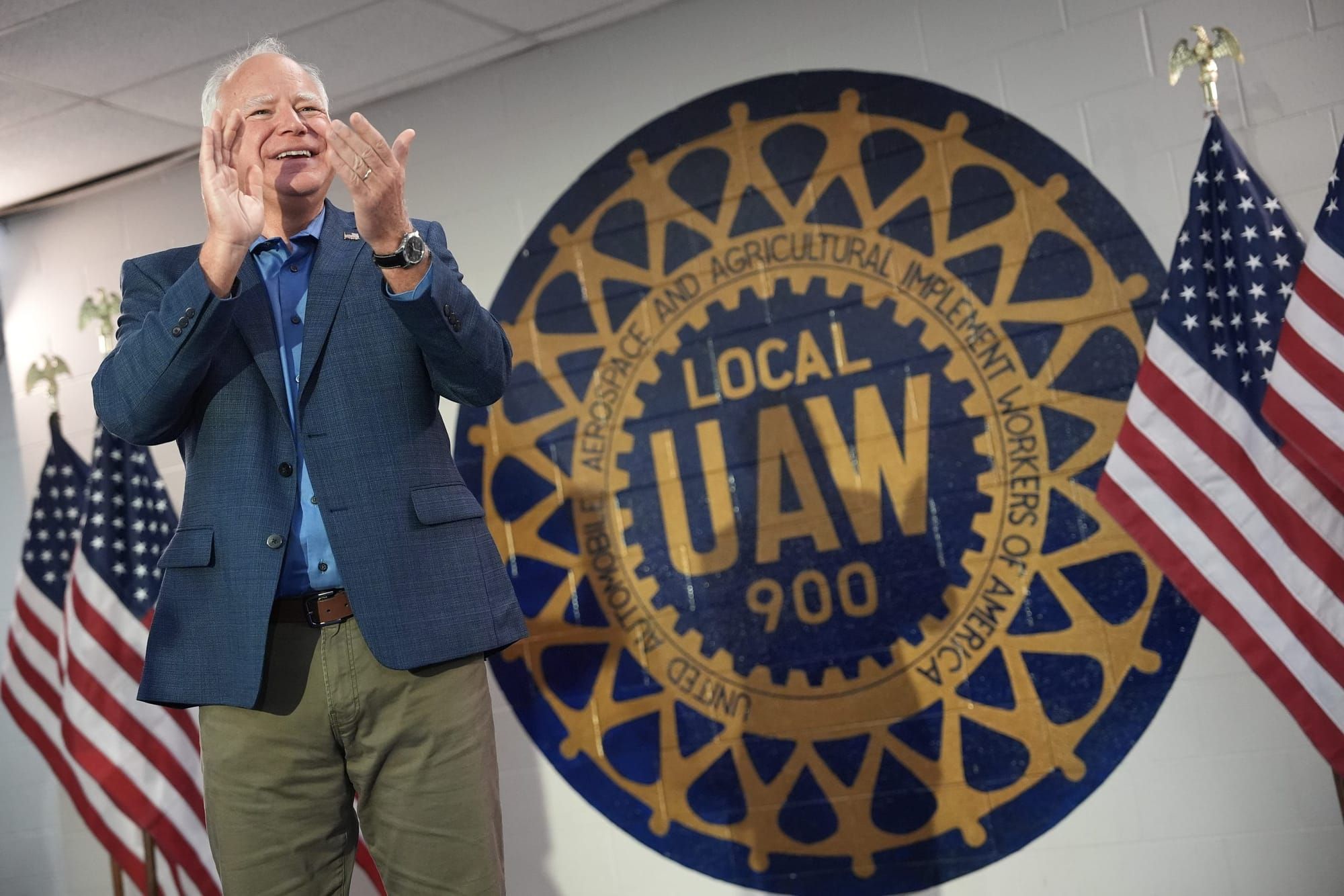 color photograph of Tim Walz standing in front of the UAW logo and two U.S. flags