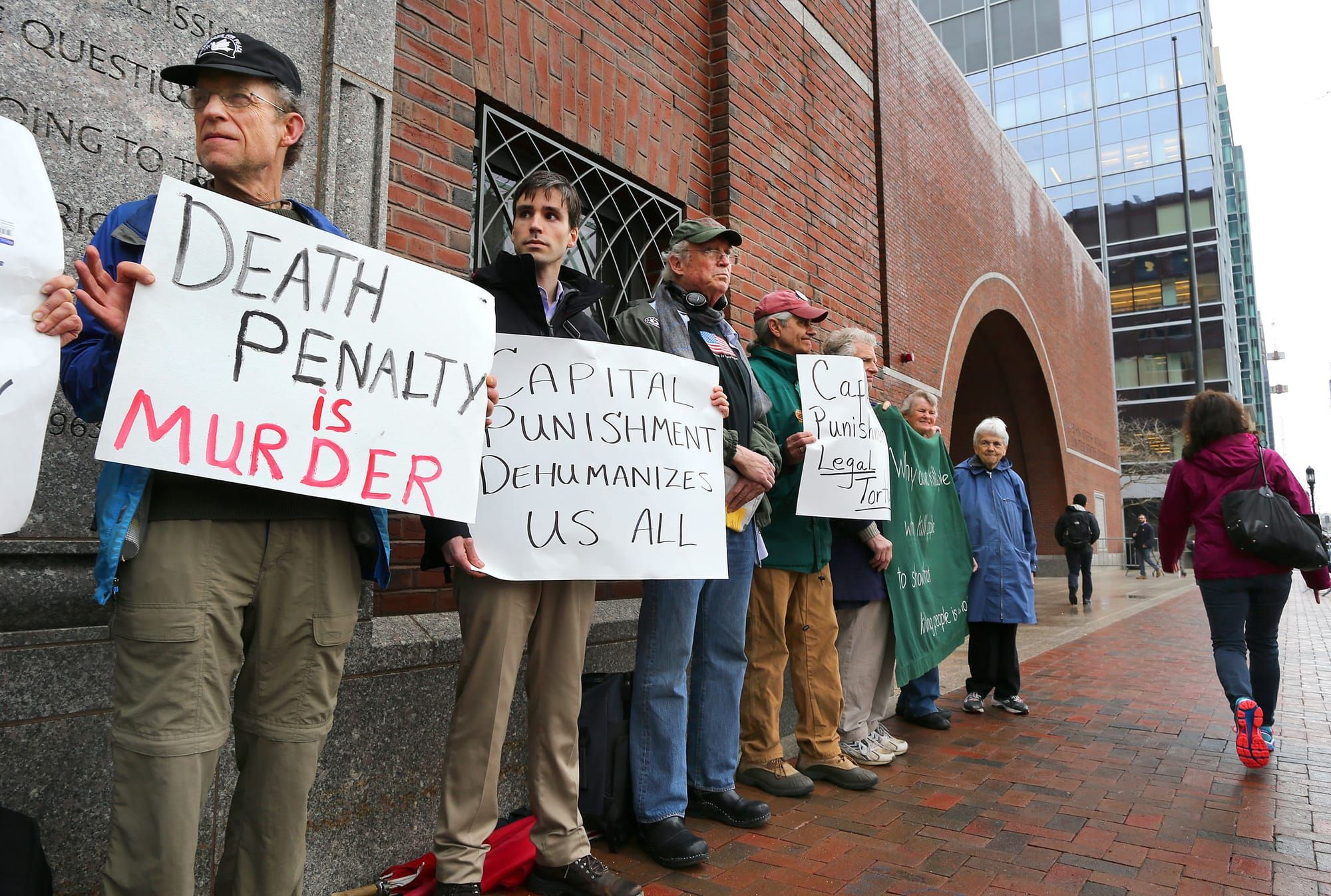 color photograph of an outdoor protest against the death penalty. people hold signs reading "death penalty is murder" and "ca