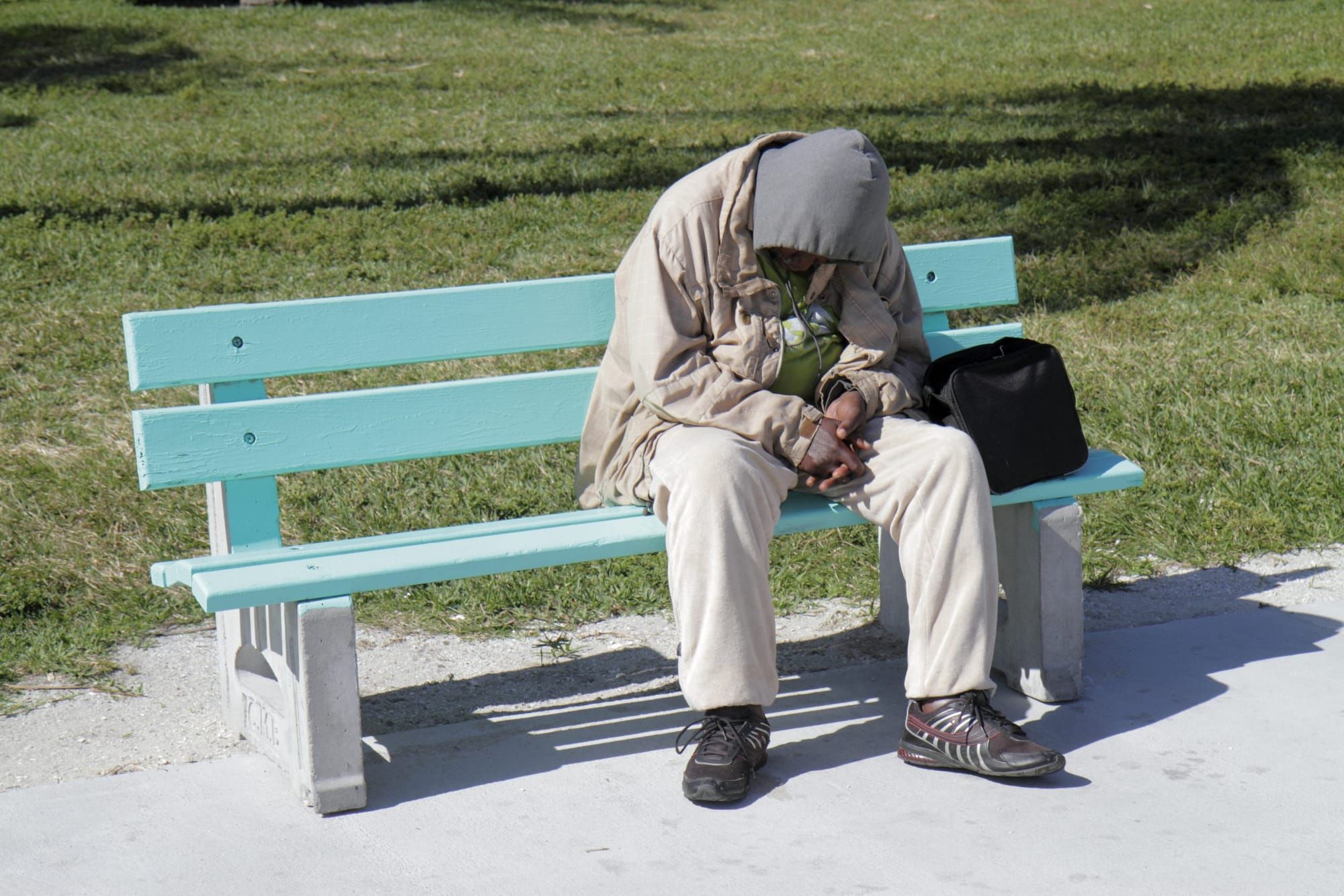 color photograph of a homeless man sitting bent over on a public bench