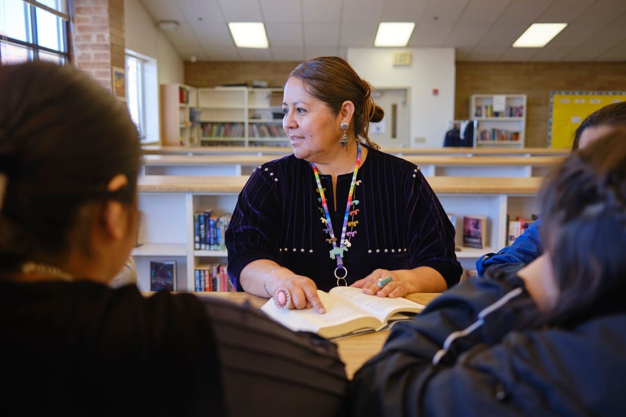 color photograph of a high school teacher with a group of students in a school library.