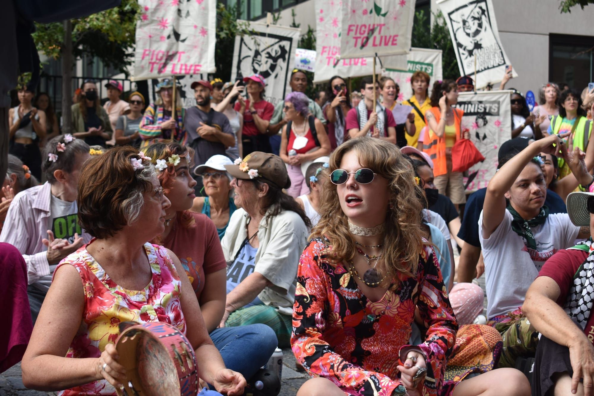 Protesters sit on the ground while some stand behind them holding up signs.