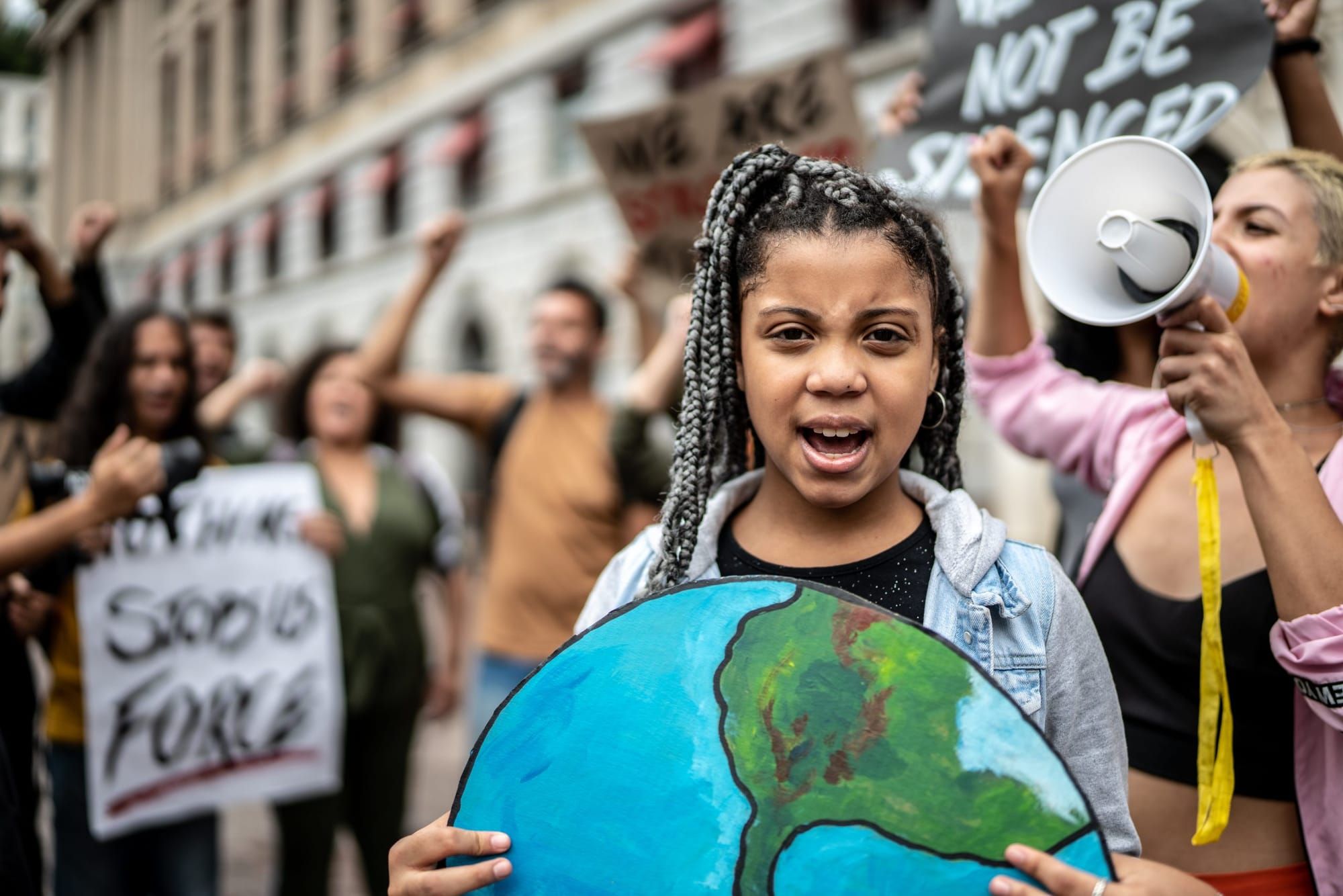 A girl stands among climate change protesters and holds a large painted picture of the earth.
