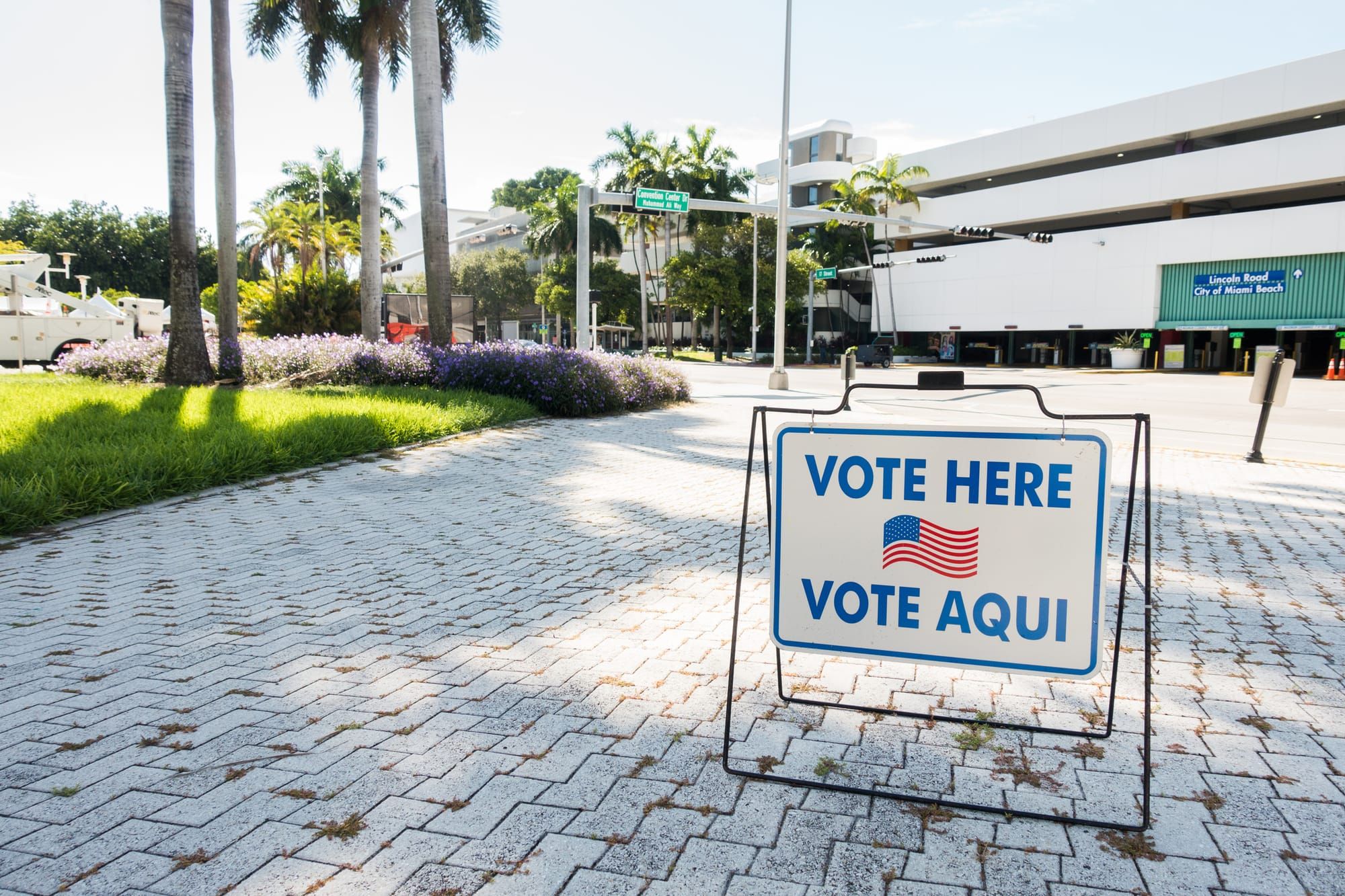 A "vote here" sign written in English and Spanish on a sidewalk near a polling place.