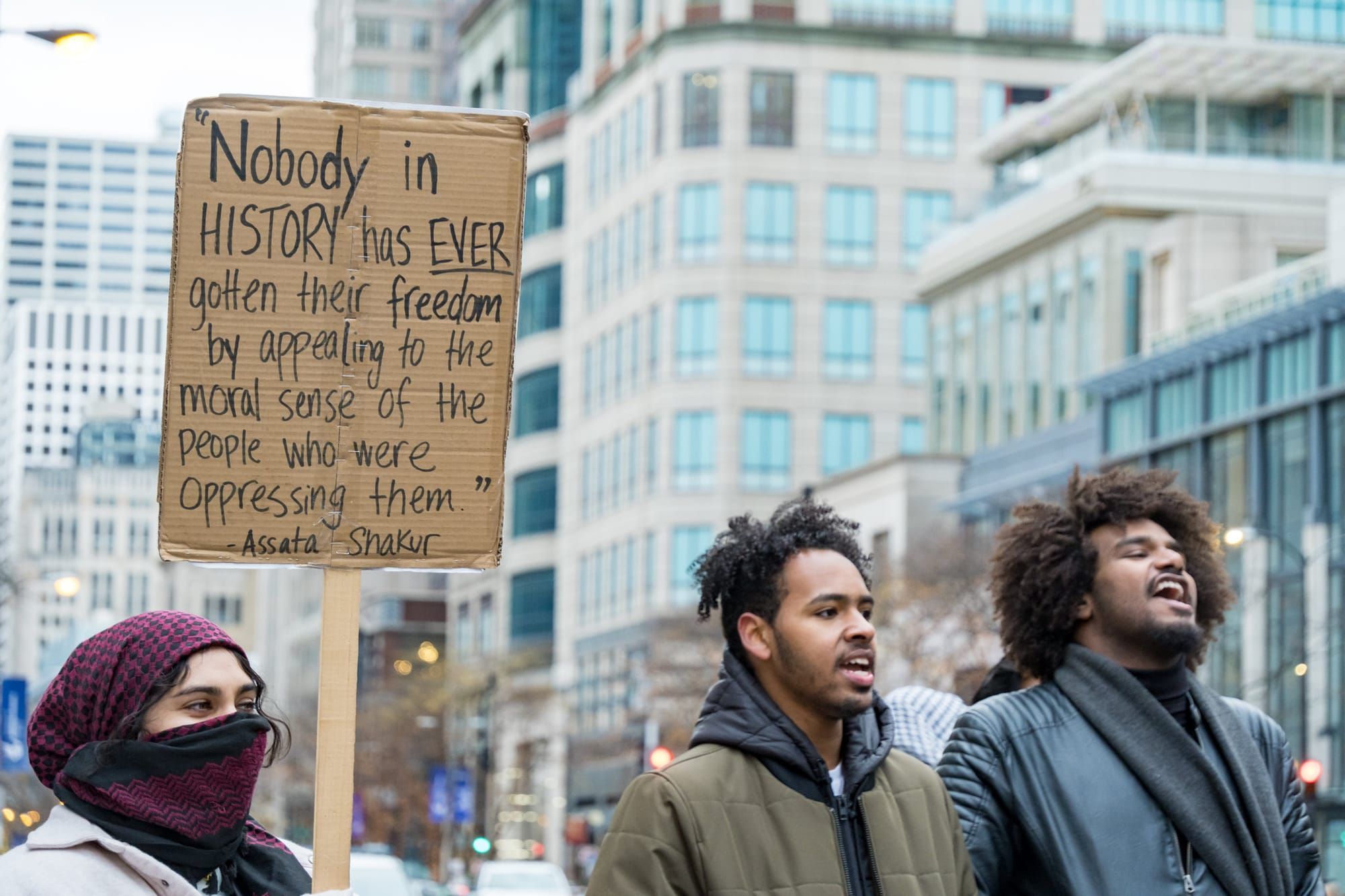 Two men chant and a woman holds a sign that reads, "Nobody in history has ever gotten their freedom by appealing to the moral