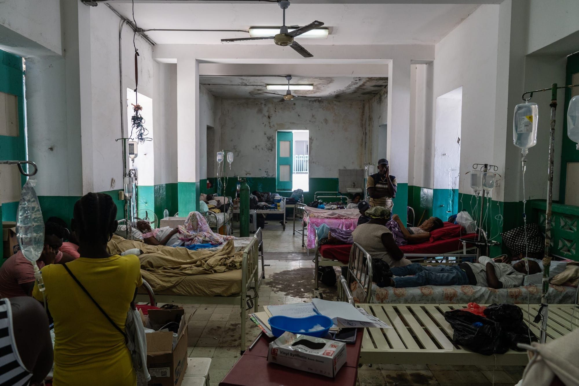 Patients lay in cots with some individuals in chairs beside them.