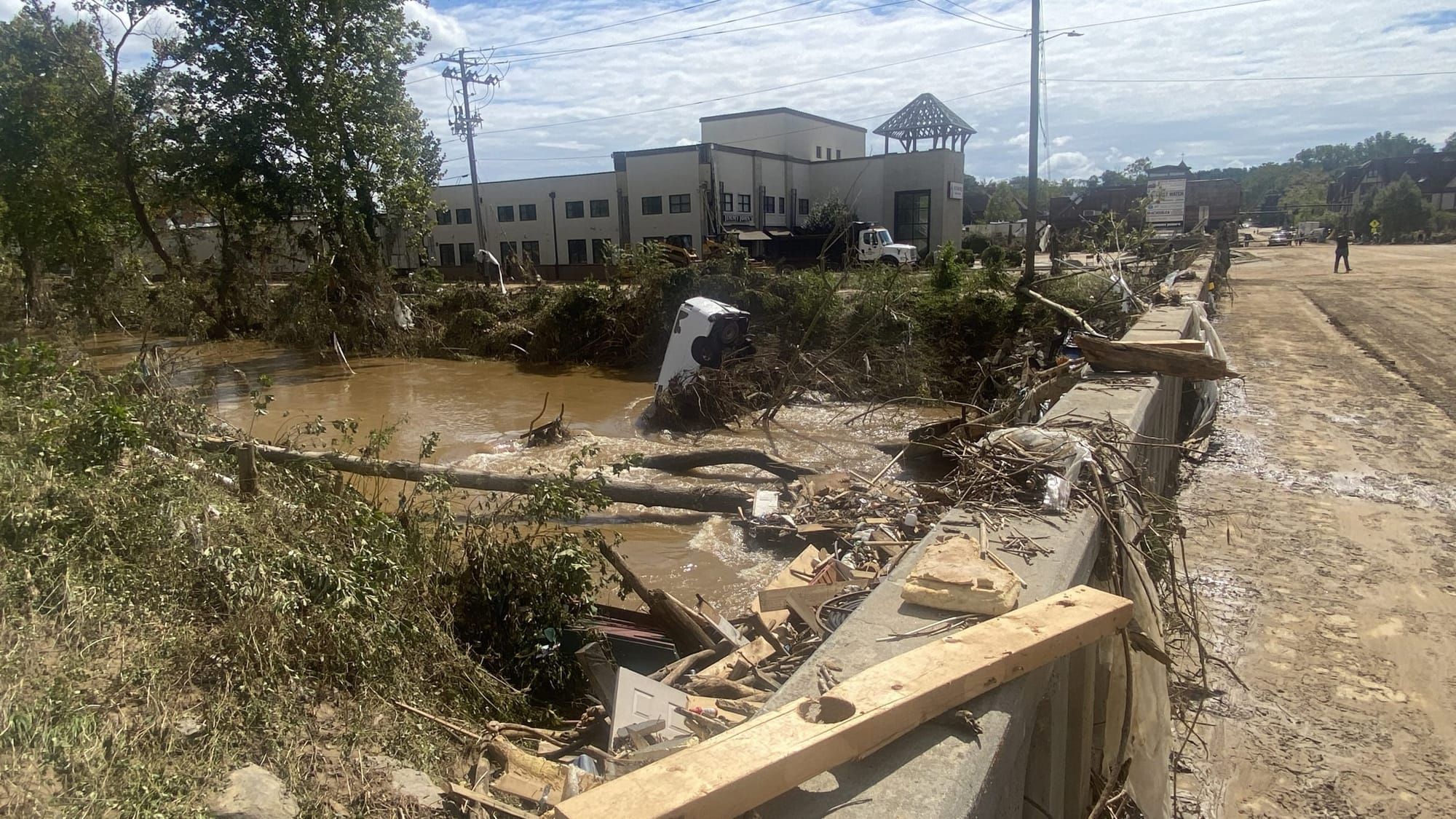 A van sits with its front end in the water and debris is strewn about near an embankment