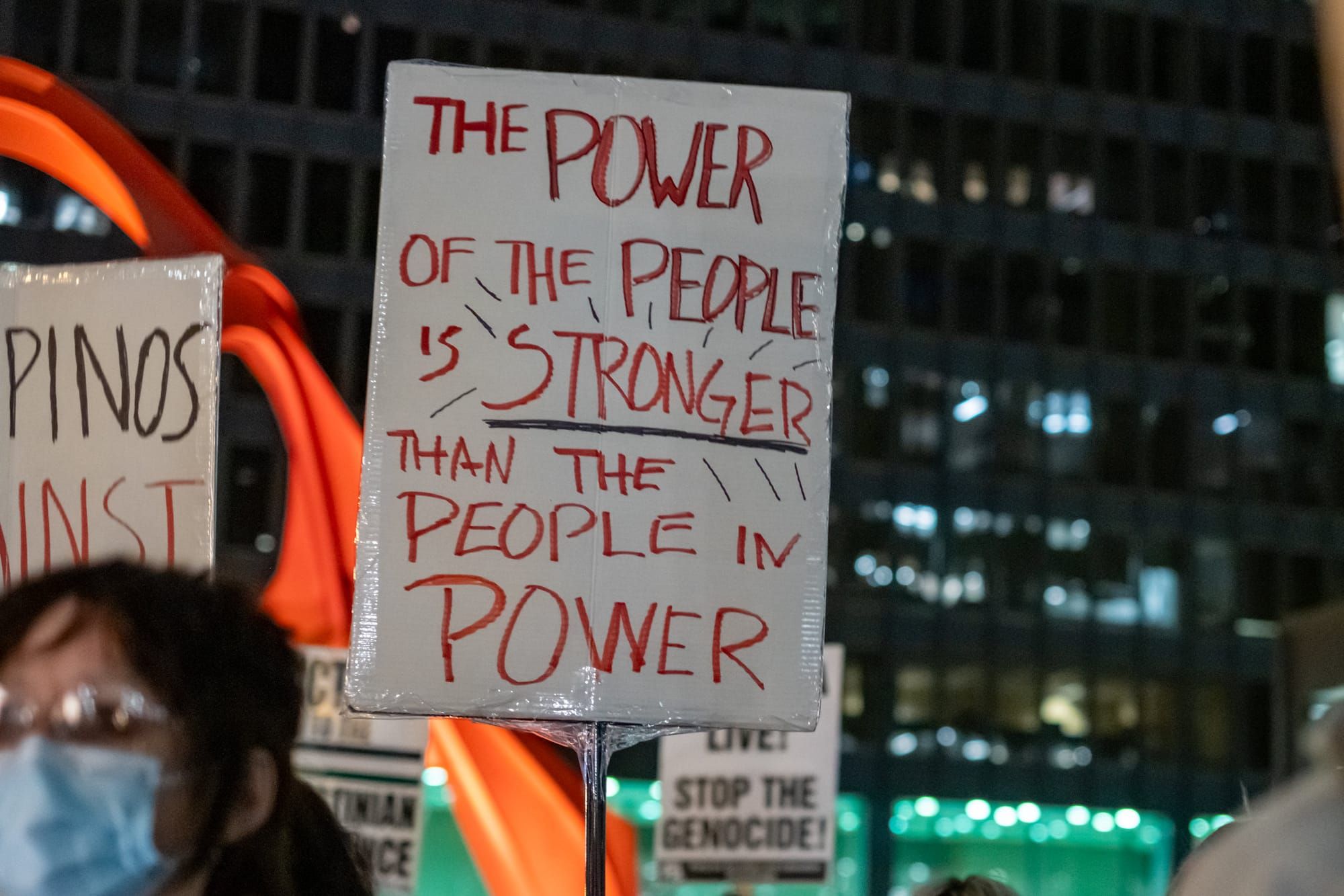 A protester holds a sign that reads, "The power of the people is stronger than the people in power." / Fascism cannot be over