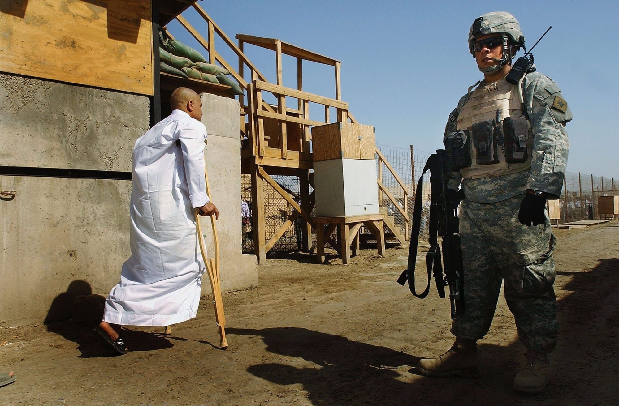 A U.S solider stands guard, looking straight forward, as a freed Iraqi prisoner walks by him on crutches at Abu Ghraib prison