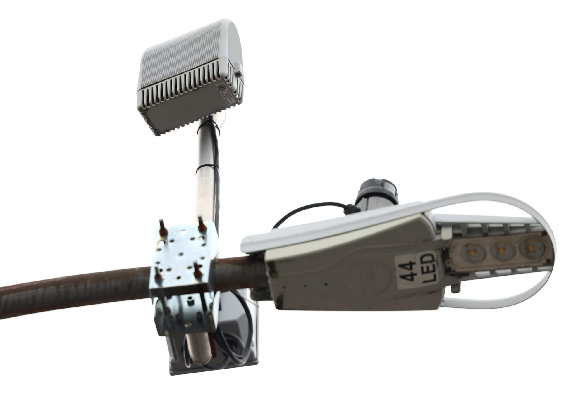 A silver ShotSpotter device is mounted on the top of a light pole.