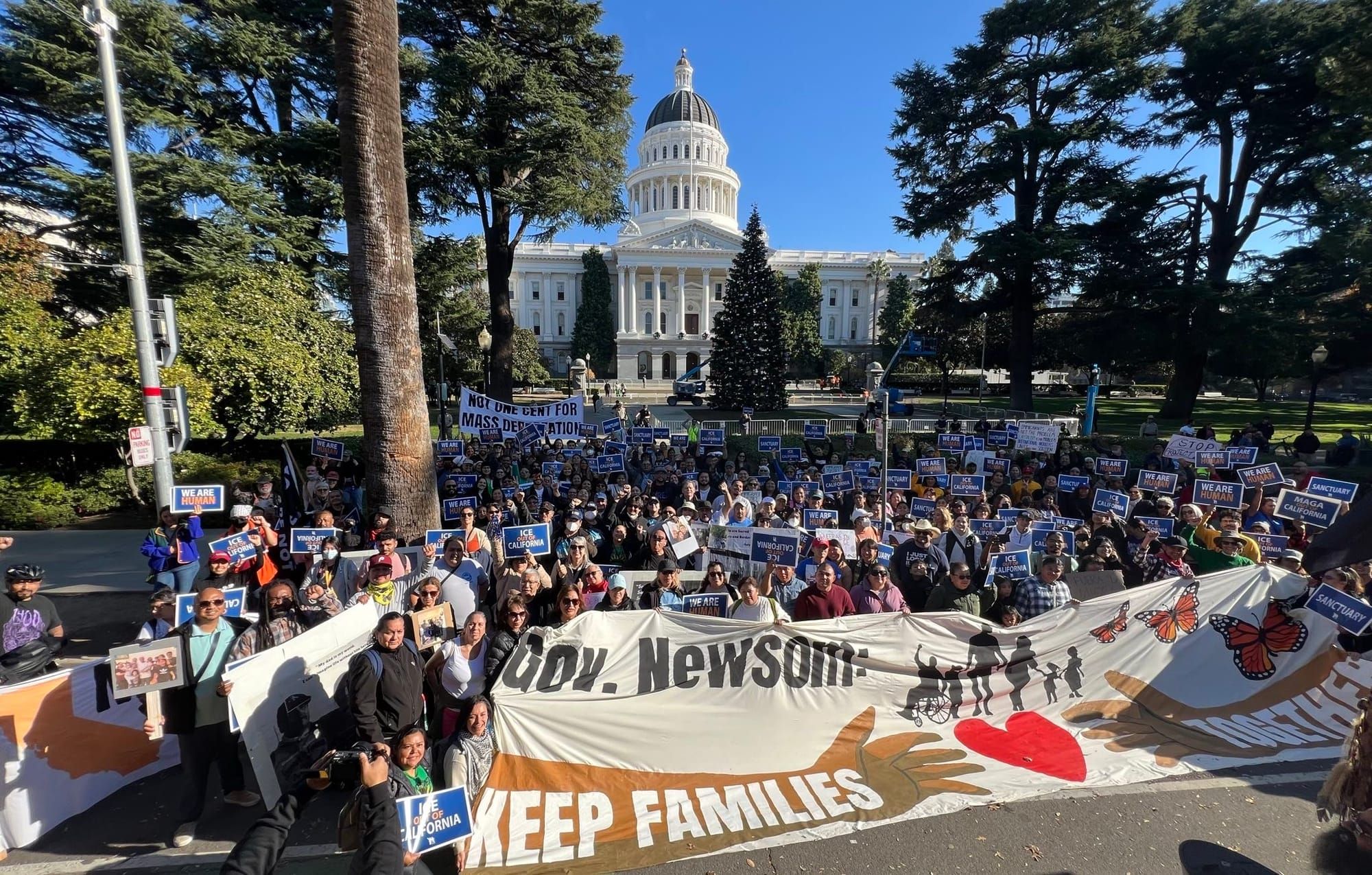 Advocates of pardons for immigrants stand as a group in front of the California State Capitol building with a sign that says,