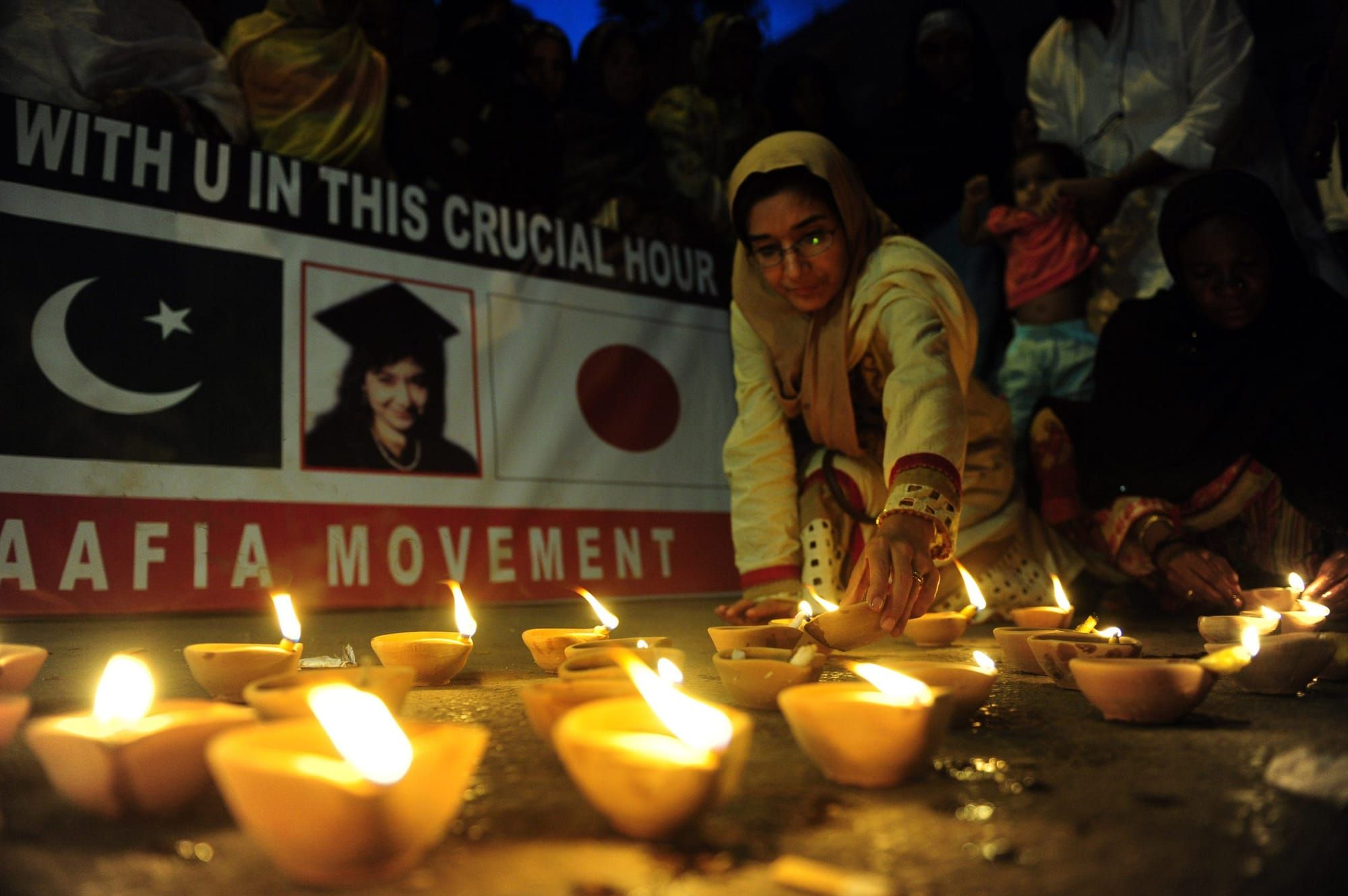 woman lights earthenware lamp among several other lamps and Aafia Movement sign in the background