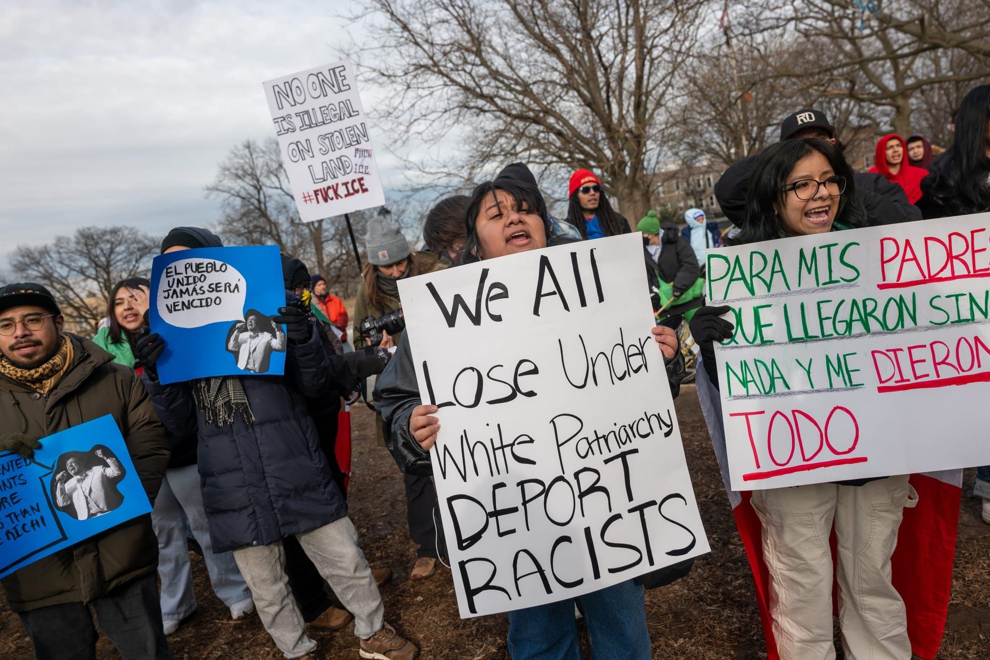 people protesting and holding signs, the sign in the center reads "We all lose under white patriarchy. Deport racists"