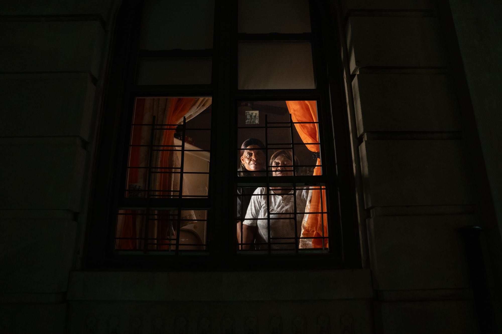 Two women look out of a window of a building where they rent apartments.