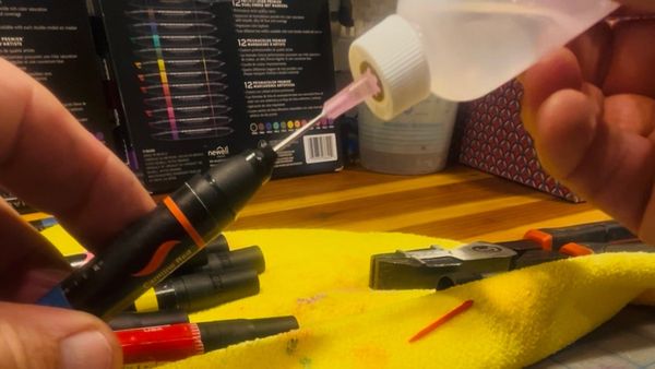 Me at my workshop, refilling Prismacolor alcohol markers. A squeeze bottle in my right hand. A marker with its fiber tip removed in my left. A rag protects the surface of a wooden workbench.