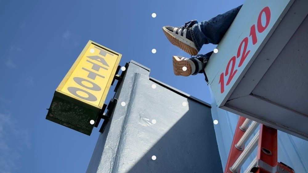 Photo of feet hanging off a rooftop and a tattoo parlor sign.