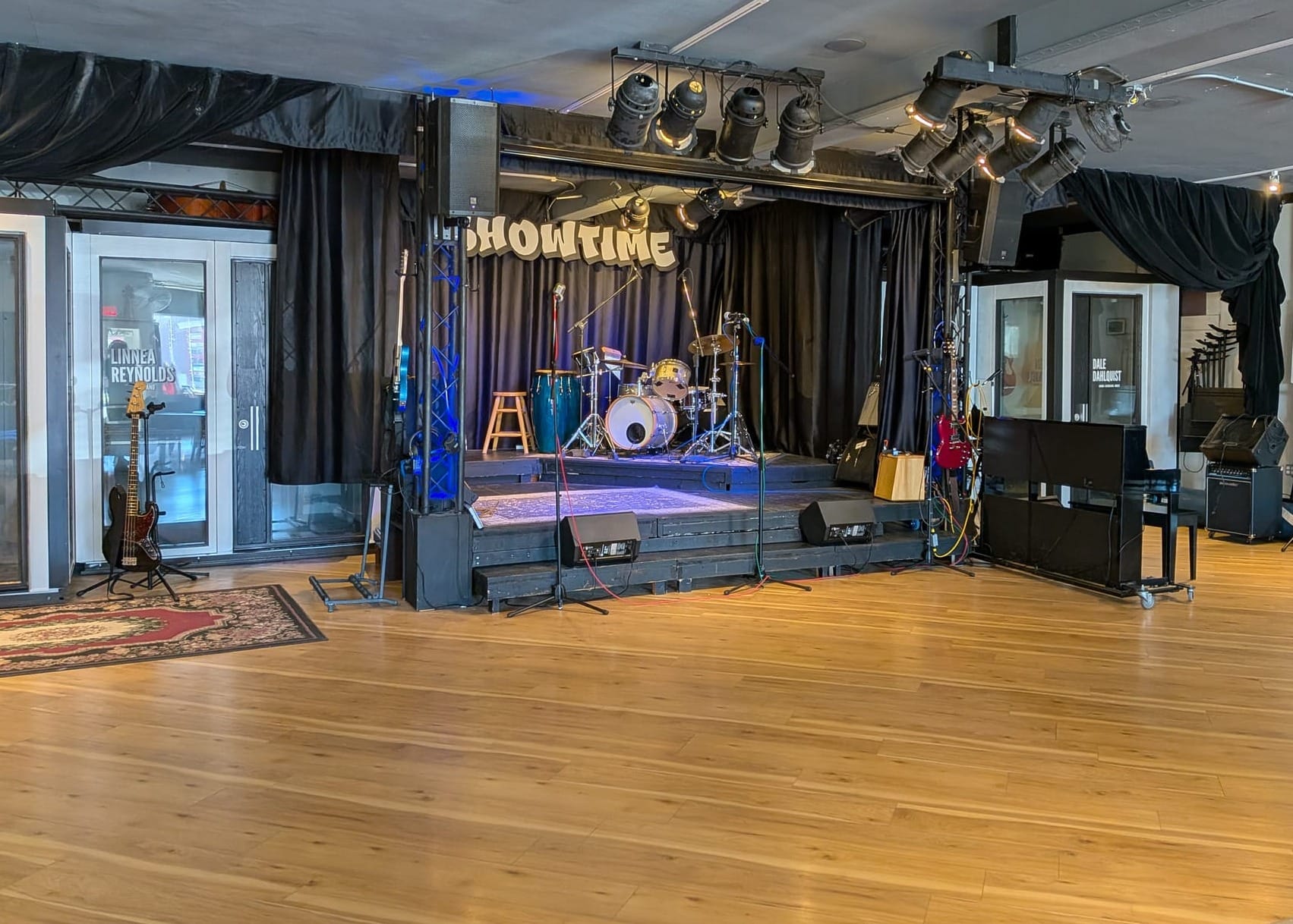 A small black stage with a drum set and microphones on it, flanked by sound booths for music lessons.