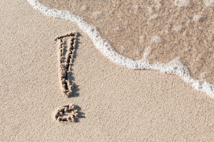 Exclamation point drawn in the sand on a beach that's about to get washed away from a wave.