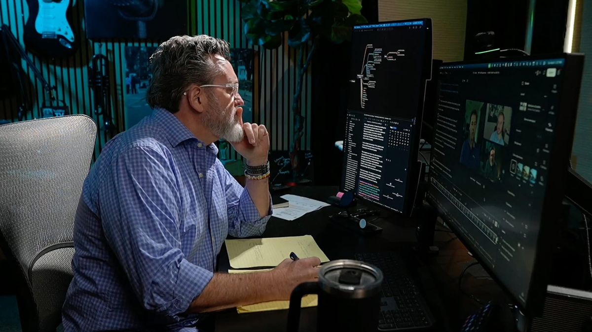 Robb Boyd sits at his desk with a pen and yellow notepad, reviewing a recorded video conversation across two monitors.