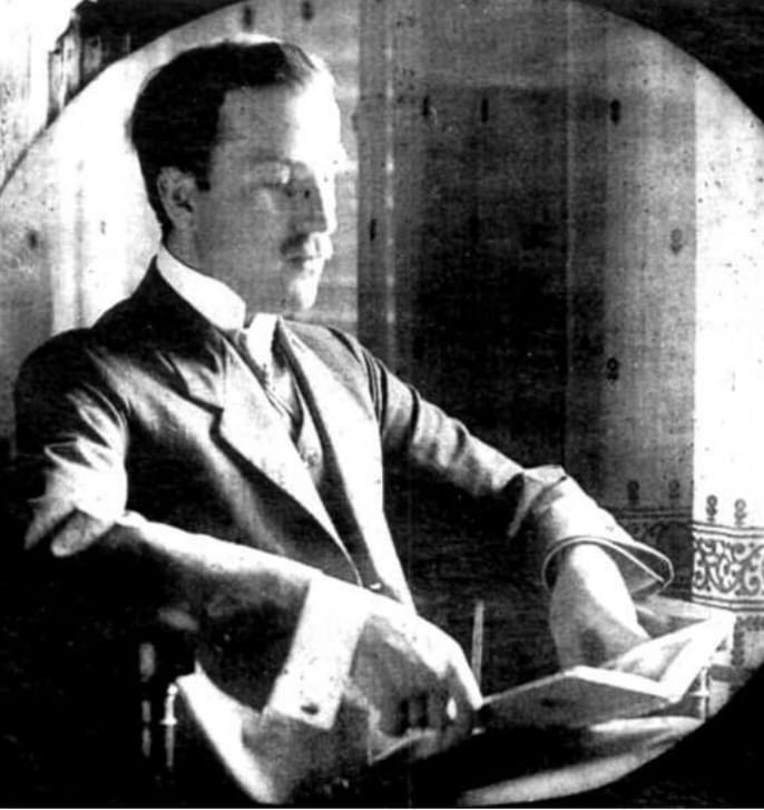 A black-and-white oval-vignette photograph of Jan Czochralski, circa 1910. A young man in a dark suit and tie sits at a desk holding an open book or papers, his head turned slightly in profile. The image is soft at the edges, characteristic of formal portrait photography of the early twentieth century.
