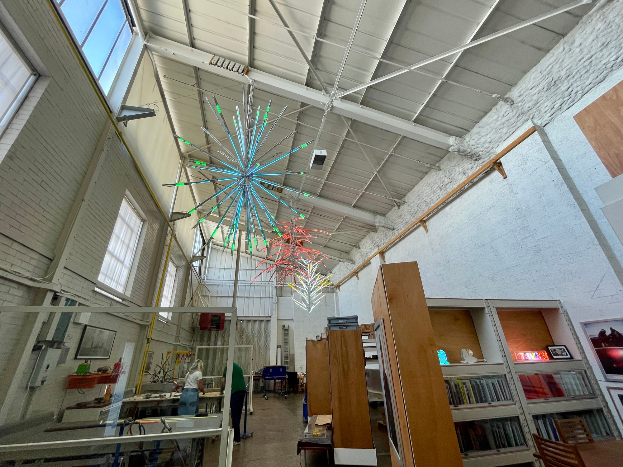 Inside Neon Workshops, a large, cavernous white space with firework-like neon sculptures hanging from the ceiling.