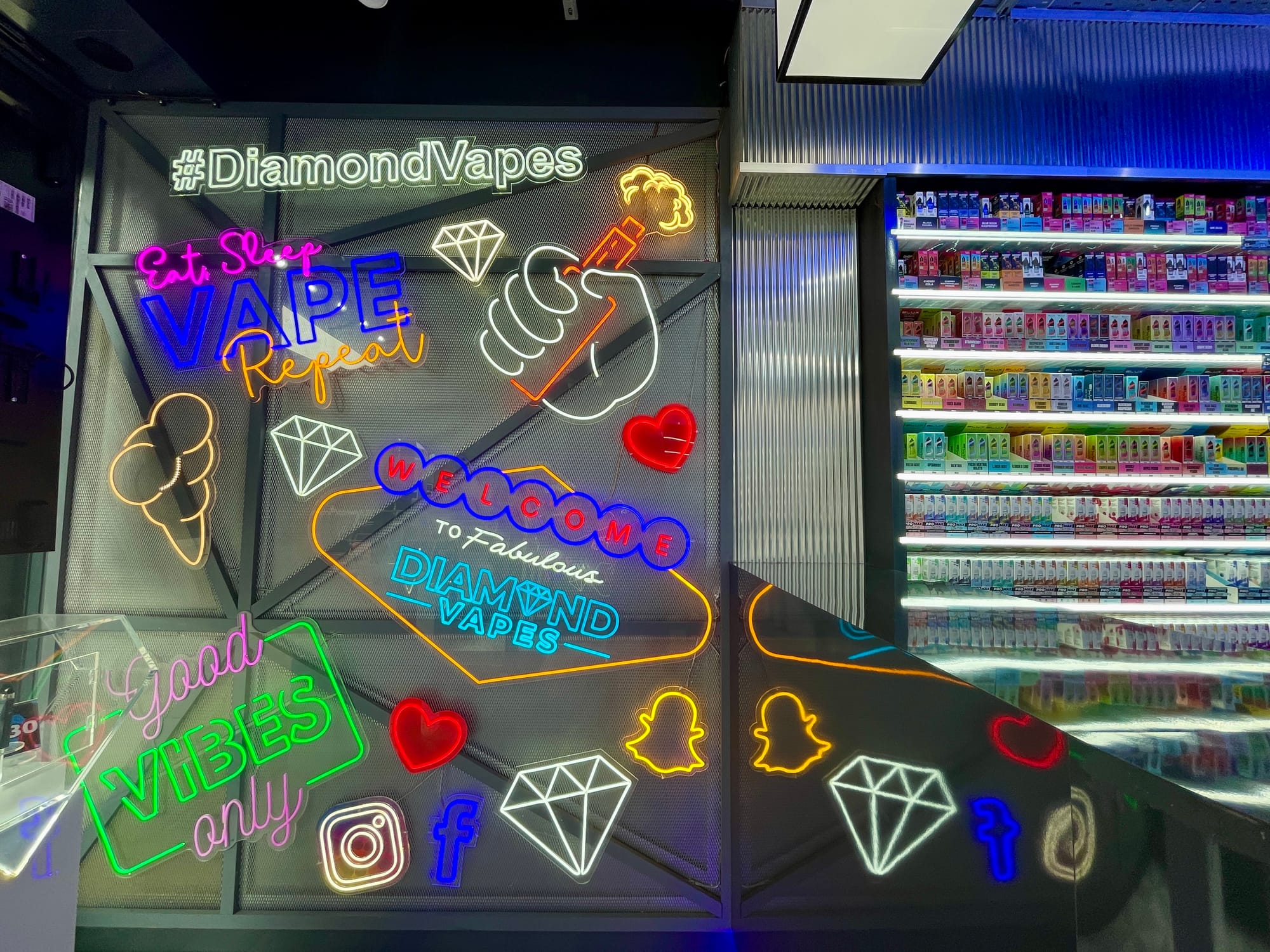 A plethora of brightly glowing multicoloured faux-neon signs in a vape shop, depicting things like diamonds and phrases like "Good vibes only."