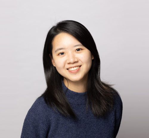 Asian young woman with shoulder length dark hair and dark blue top smiling.