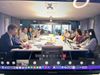A computer screen showing a Zoom meeting with a large table circled by people in discussion.