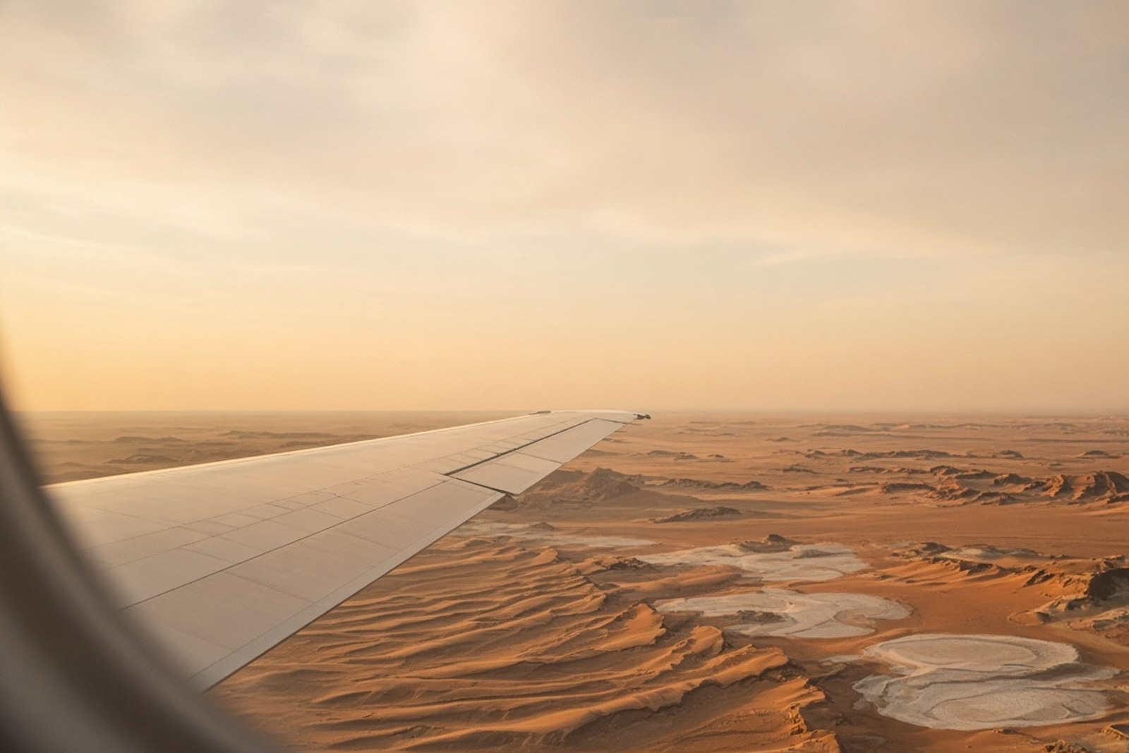 Golden hour light over a desert and salt flats, seen from an aircraft window.