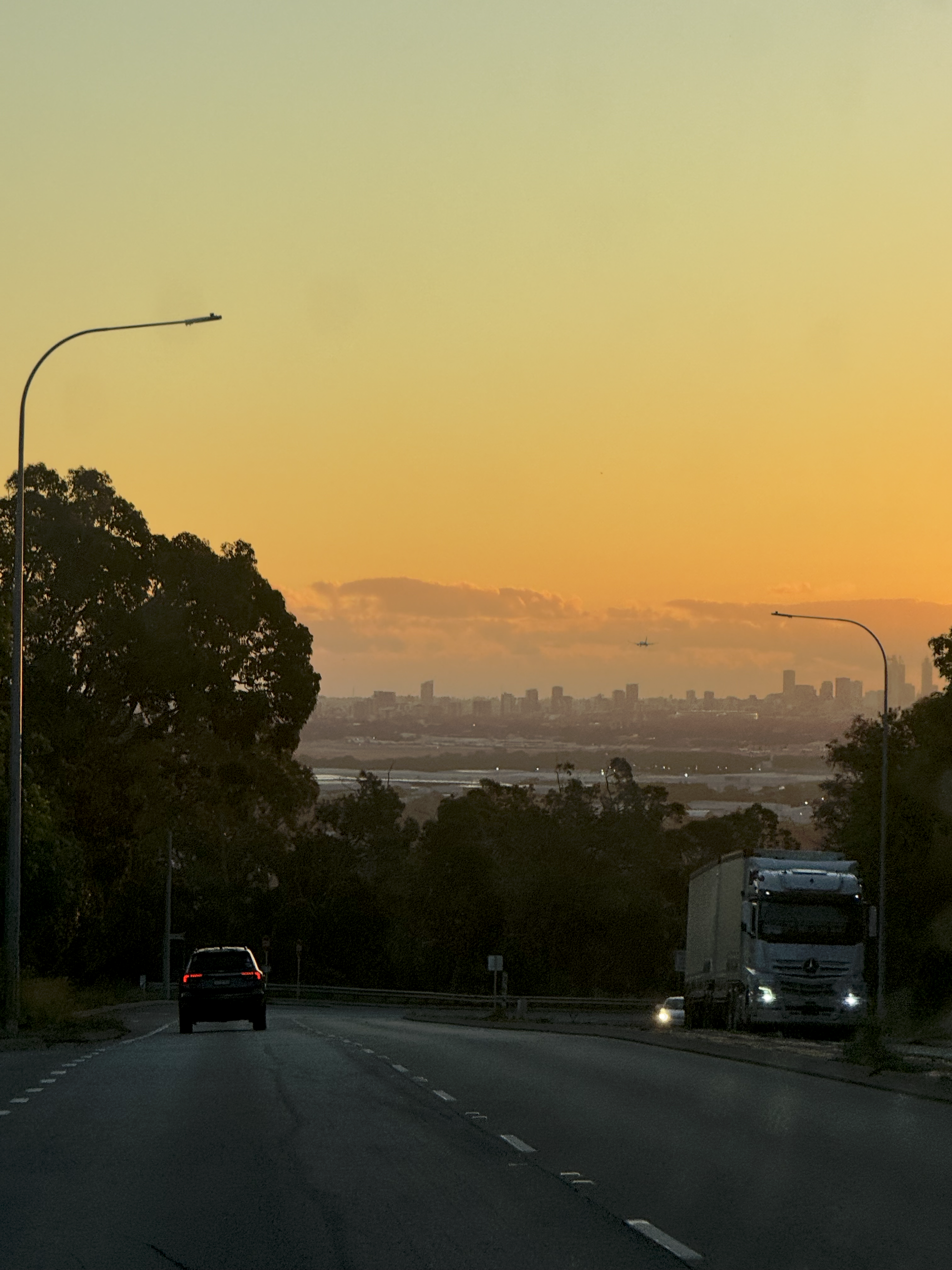     The road down into Perth at sunset, with the city skyline under an orange sky.