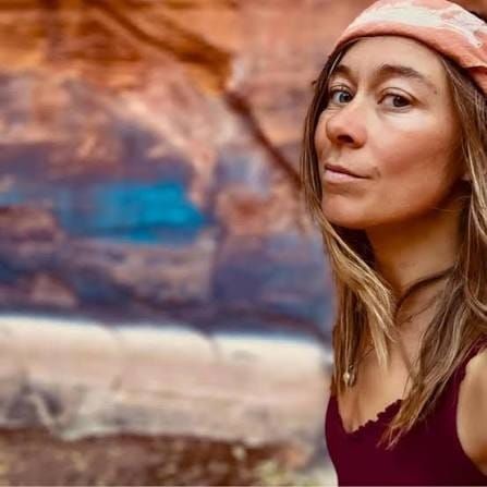 A young woman looking sidelong at the camera, with a background of Utah red rock.
