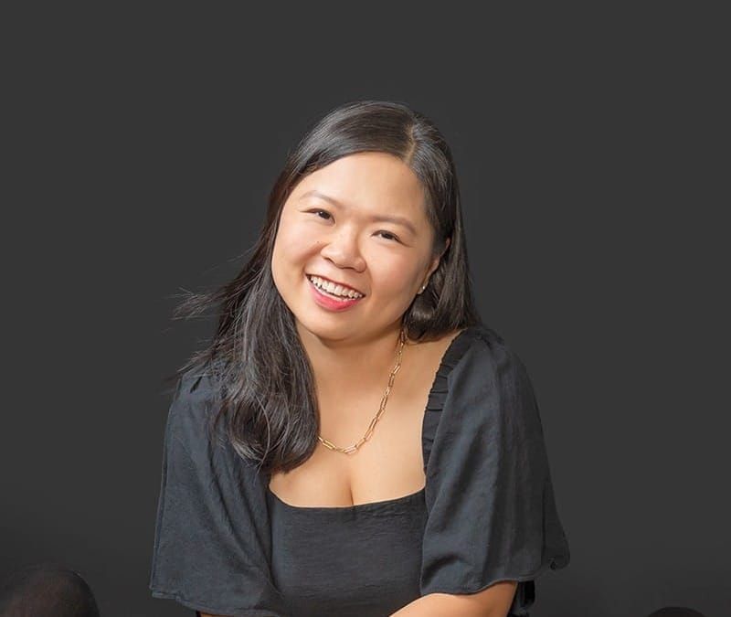 Lina Lie, gentle parenting coach, smiling and seated in a black dress against a dark background.