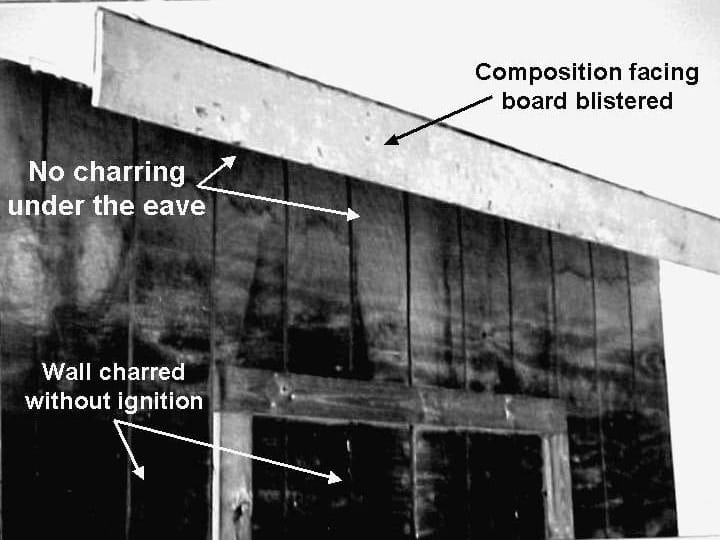 Charred wood wall section after a crown fire, with an unburned band where the eave shaded the wall