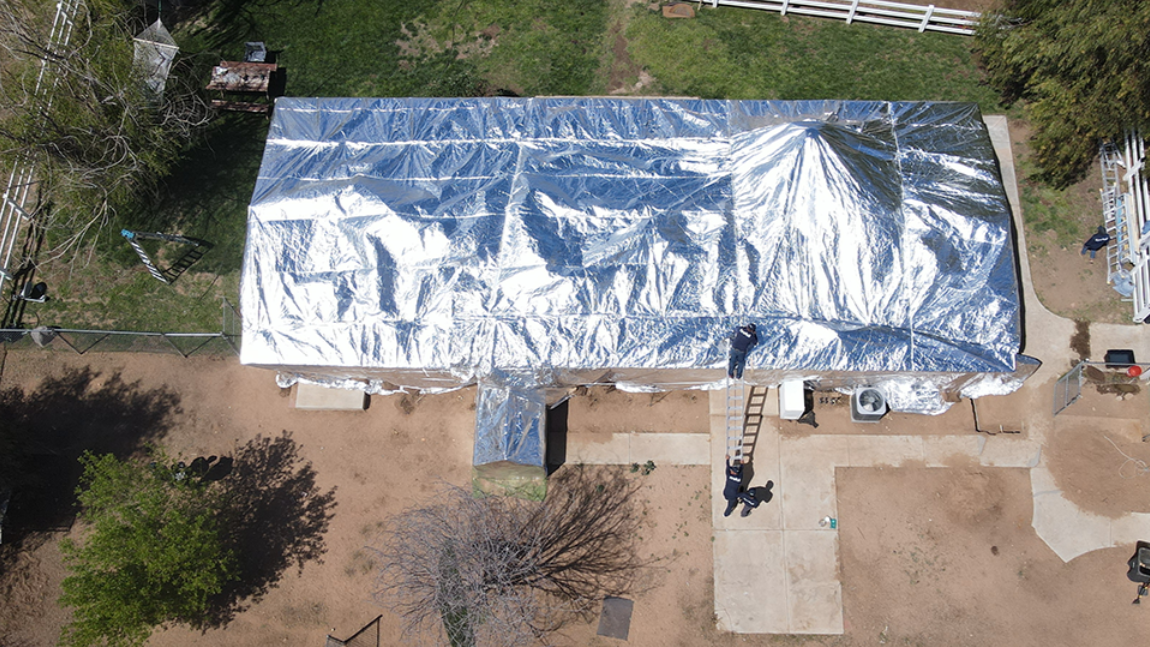 Aerial view of a single-story home covered in reflective structure wrap