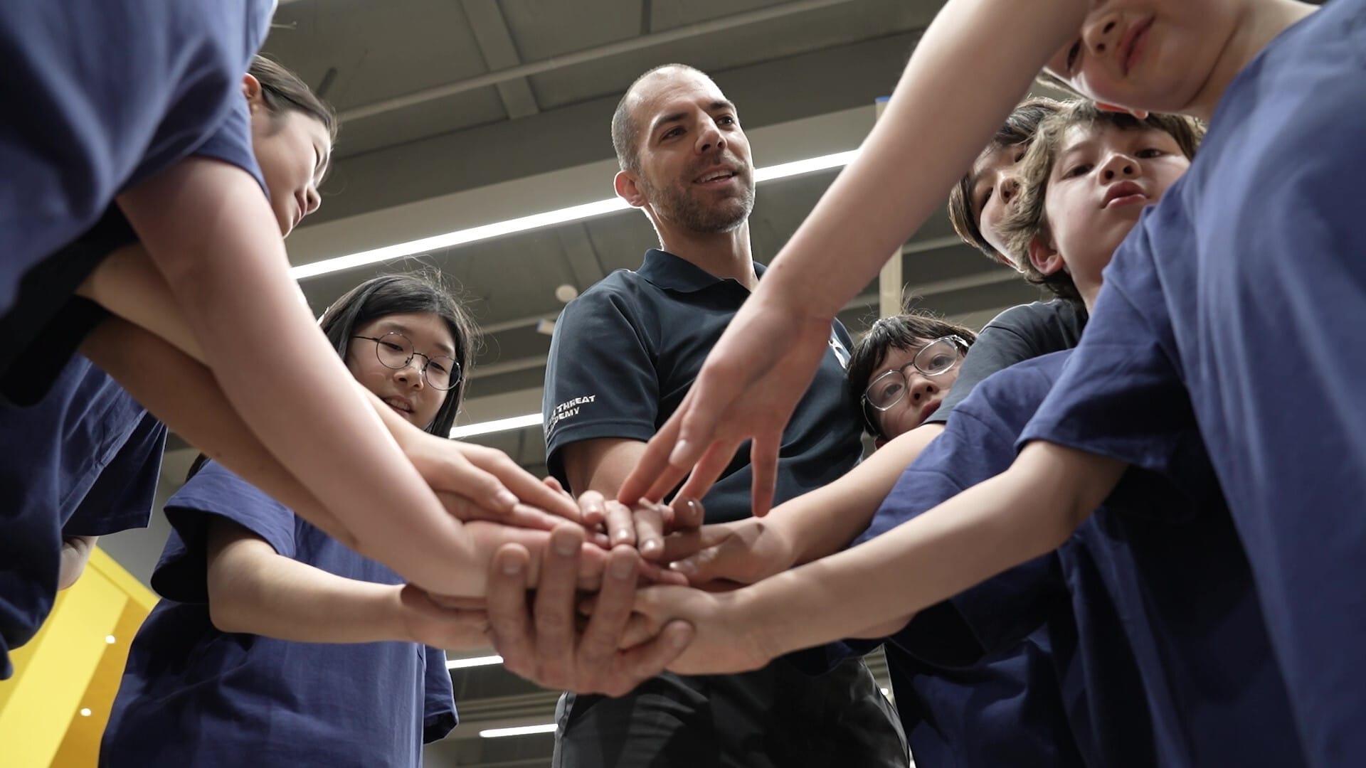 Teacher and middle school students at Seoul Providence School join hands in a team huddle, promoting unity and encouragement
