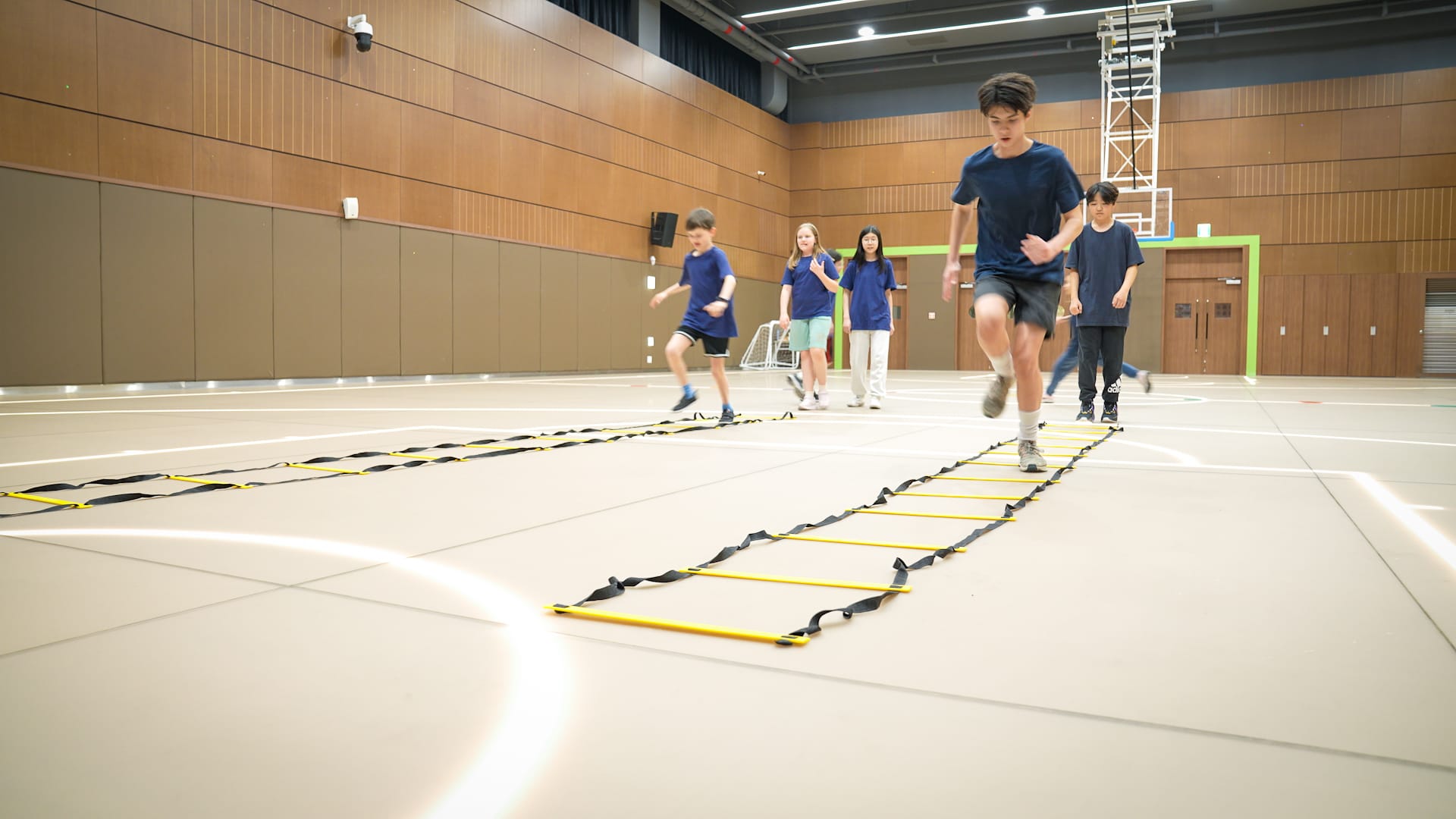 Middle school students doing agility ladder drills in a gym at Seoul Providence School, guided by instructors