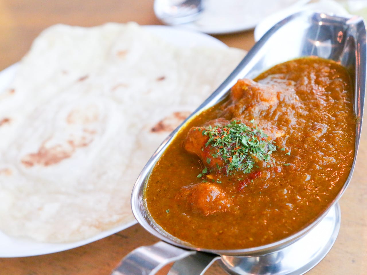 Close-up of spicy Indian chicken curry with herbs, served with fresh naan at Rama & Bavana Dongseongno in Daegu