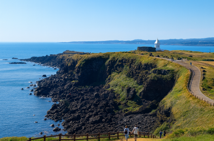 Jeju Seopjikoji coastal cliff with walking path and lighthouse overlooking the blue ocean on a clear sky day