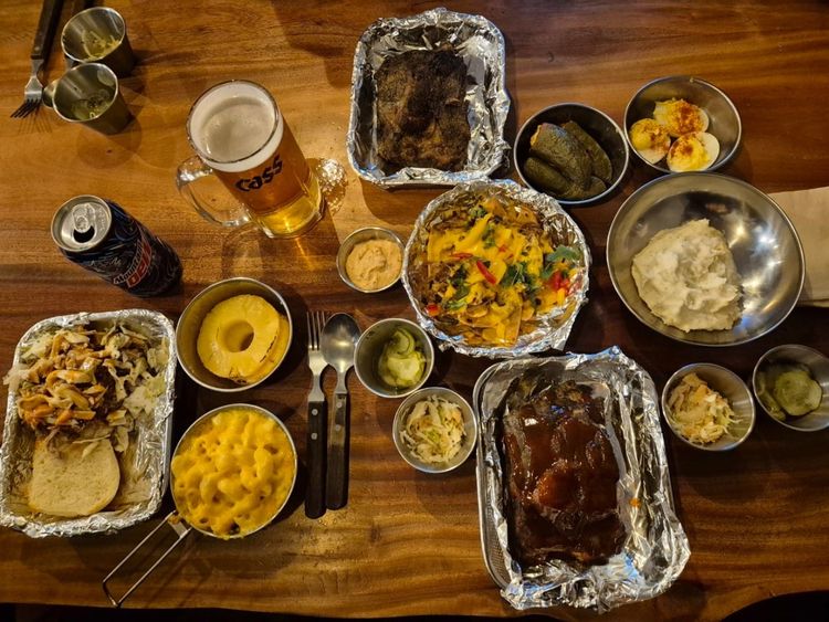 Southern BBQ feast with ribs, pulled pork sandwich, mac and cheese, mashed potatoes, pickles, deviled eggs, grilled pineapple, beer and soda at Sunday Best restaurant in Korea