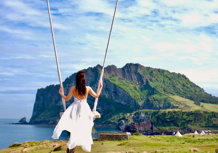 Tourist enjoying a swing at Haeilri Café with Seongsan Ilchulbong sunrise peak view in Jeju, a popular stop for Jeju car rental travelers