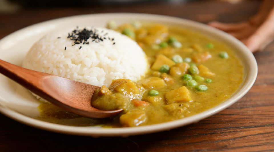 A plate of vegetarian curry with white rice and green peas, served with a wooden spoon on a table