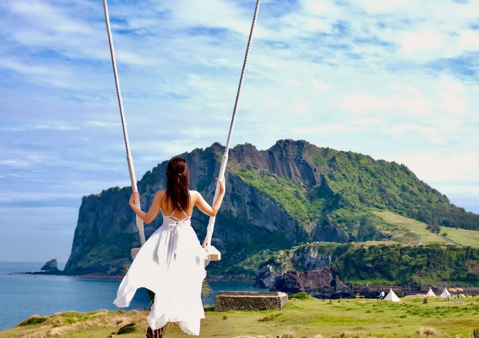 Tourist enjoying a swing at Haeilri Café with Seongsan Ilchulbong sunrise peak view in Jeju, a popular stop for Jeju car rental travelers