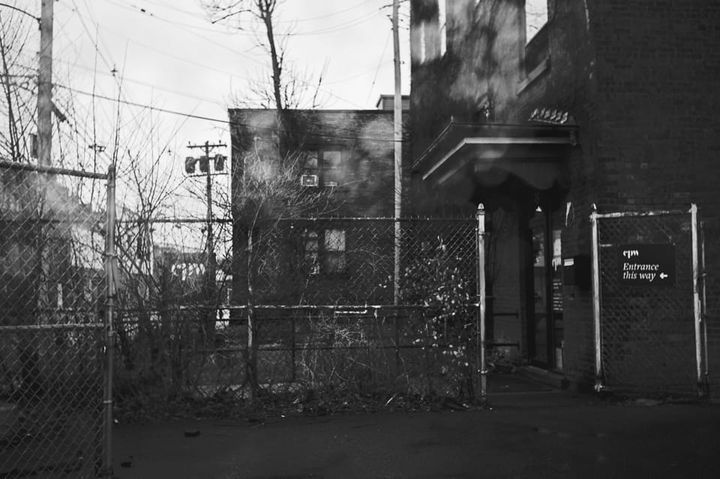Side view of the entrance to Center for Photography Kingston, on a cloudy rainy day in black and white. There's a fence on the side of the building, with buildings in the background.