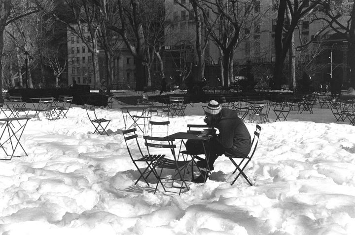 A person sitting at an outdoor table, eating, with mounds of snow all around them.