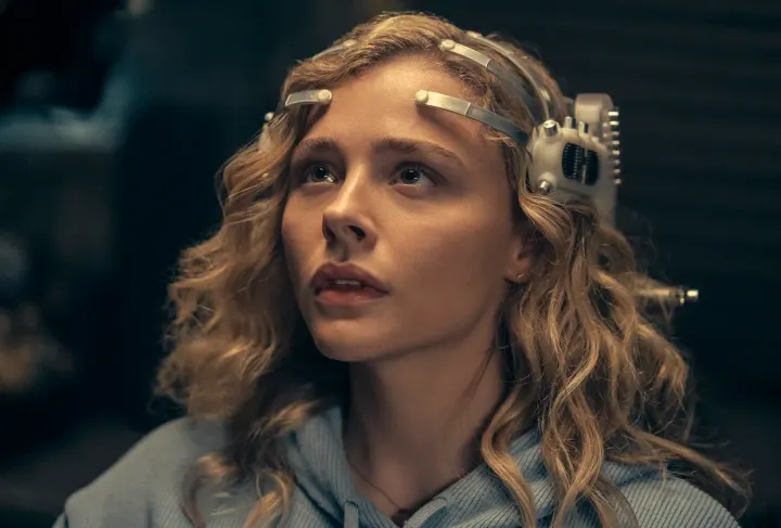 A blond woman stares to the left side of the frame. She has a plastic and metal device on her head.
