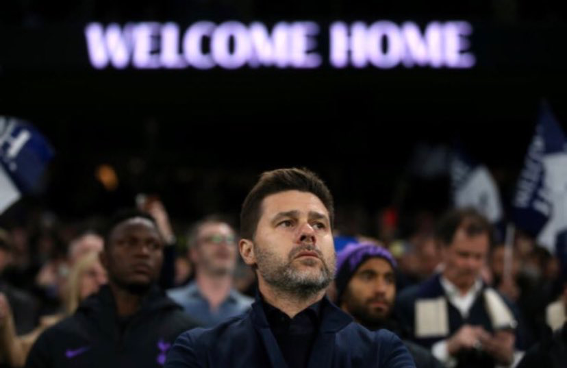 Mauricio Pochettino stands with a sign in the stadium that says "welcome home" behind him in the background.