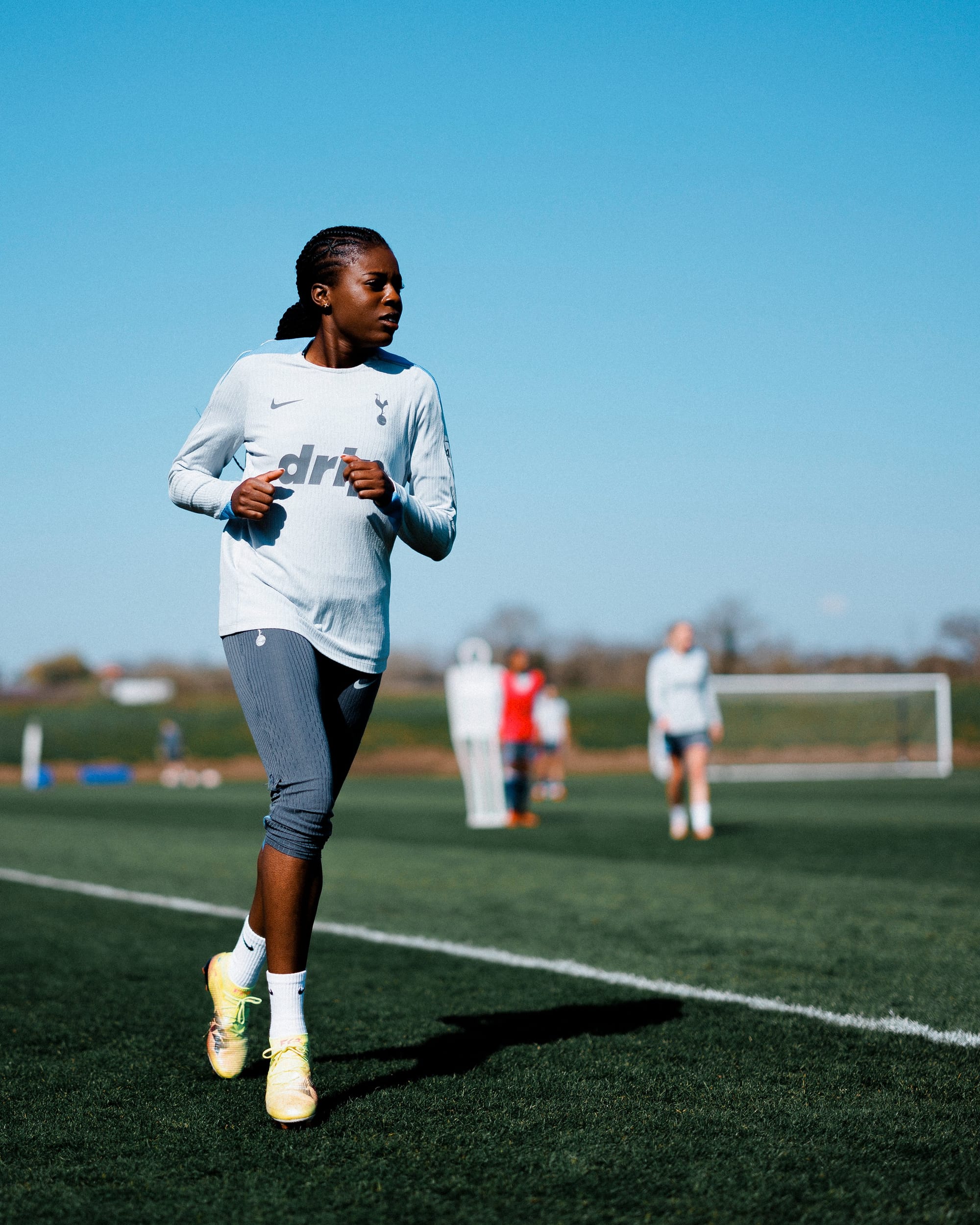 Jess Naz runs at the training ground with a few teammates blurred out in the background.