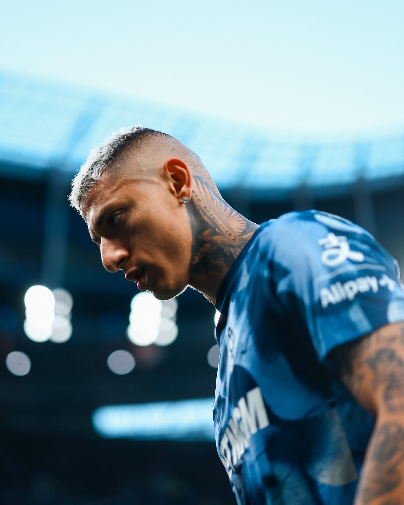 Richarlison looks focused during warmups in a photo shot from below, the stadium blurred in the background.