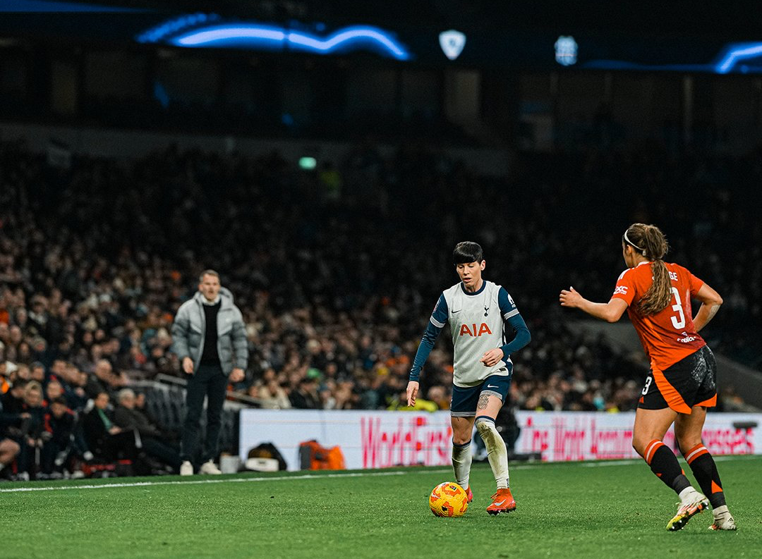 Ash Neville dribbles the ball as Gabby George approaches, Robert Vilahamn shouting on the sideline in the background.
