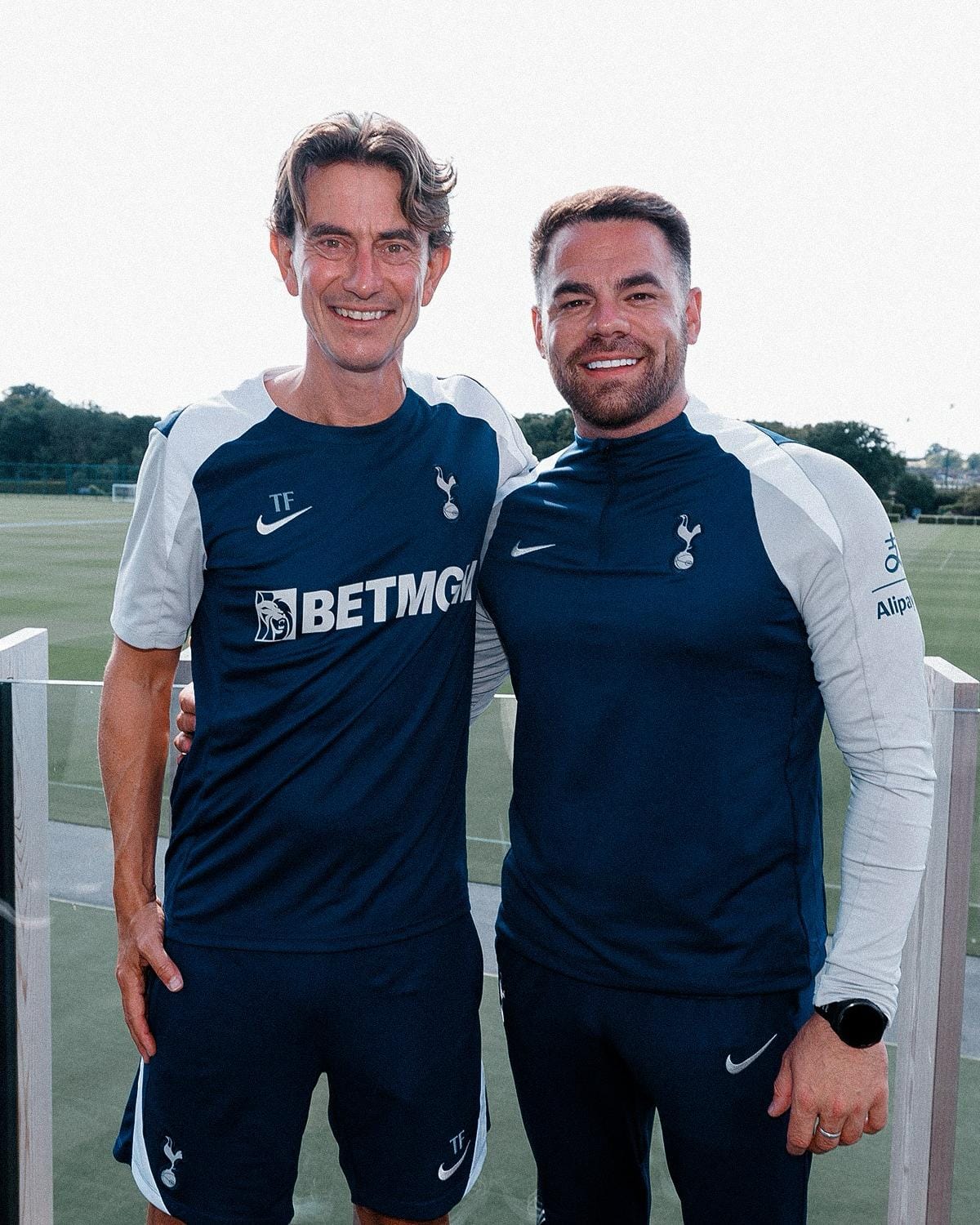 Thomas Frank and Martin Ho pose for a photo with their arms around each other, wearing navy and gray training gear.