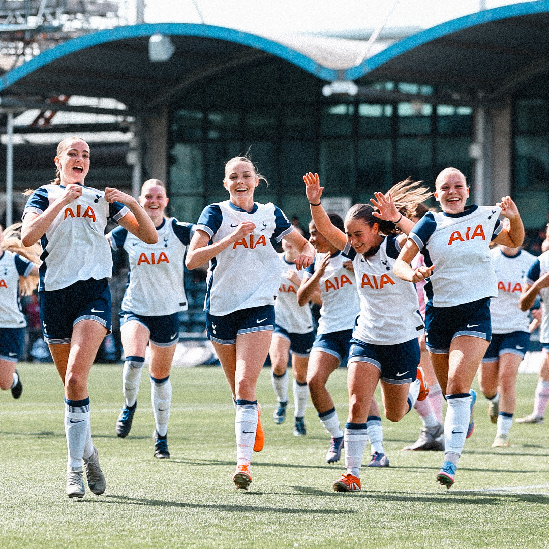 U17 players run to celebrate their trophy win, several holding up the Tottenham badge on thier kits.